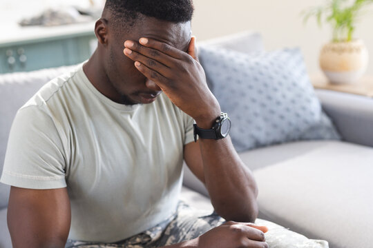 Troubled african american male soldier sitting on couch at home, holding head, copy space