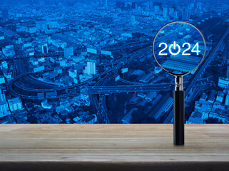 2024 start up flat icon with magnifying glass on wooden table over modern city tower, street, expressway and skyscraper, Business happy new year 2024 success concept