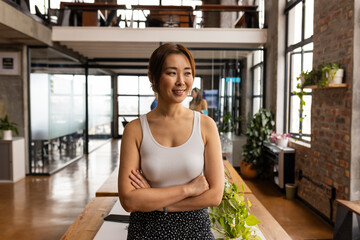 Confident Asian woman stands in a modern office, exuding casual business professionalism
