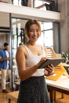 Asian woman in a casual business office setting, holding a tablet
