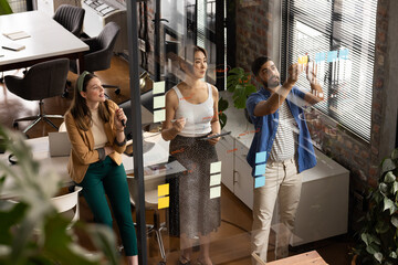 Young Asian man explains a concept on a glass wall in a casual business setting in the office