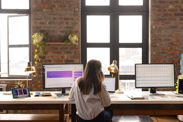Young Caucasian woman works at a dual-monitor desk setup in a casual business office