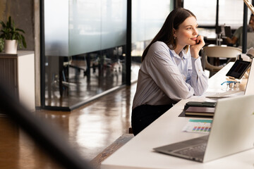 Young Caucasian woman sits thoughtfully at her casual business office desk
