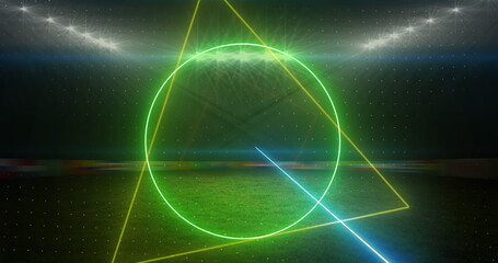 Image of rotating neon shapes and lights over floodlit sports field