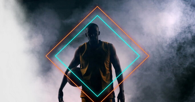 Image of orange and blue neon diamonds over african american male basketball player holding ball