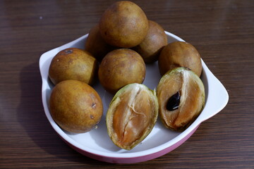 several ripe sapodilla fruits that have been cut in half on a plate.