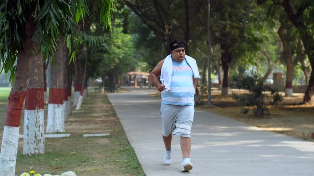 Indian man gets tired after a morning jog - healthy lifestyle  sweating  overweight  summer morning. Obese man running in the park - running track  outdoor workout  out of breath  persistent motiva...