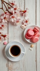 Top view of cup of coffee and peach macarons and pink spring flowers on wooden table