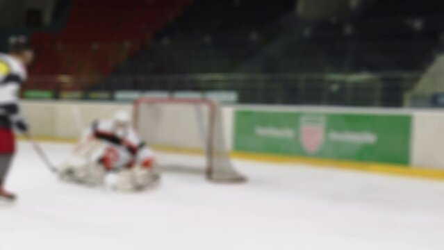 Ice hockey player attacks, forward makes wrist shot, puck flies between goalie's leg pads, attacker scores, keeper makes butterfly movement, goaltender drive knees down but misses goal. Blurred