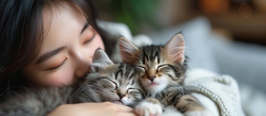 A happy woman cuddles two small to medium-sized cat kittens in her arms, feeling their soft fur and admiring their whiskers as they enjoy the grass together.