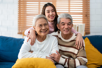 Portrait of Asian senior couple sitting on sofa with daughter in house. 