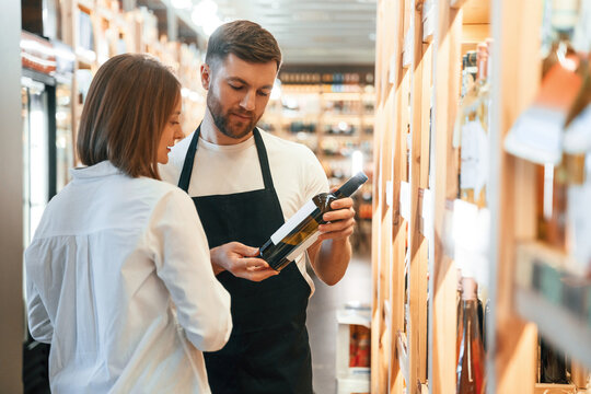 Asking for help. The shop owner helps a young woman to choose a good wine