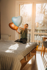 A boy in a green T-shirt with an orange and blue balloons in the shape of a heart on the bad. Valentine's Day. Portrait of a child. Front view