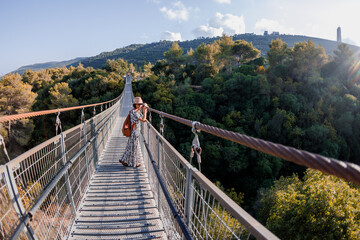 young girl in a hat stands on a suspension bridge and looks dreamily into the distance.