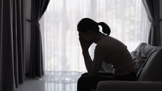 Silhouette of a person suffering from depression in the house, Depressed woman sitting alone on the Sofa feel stress, sad and worried in the dark room. person are stressed.