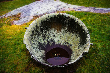 Large Rustic Lichen-covered Broken Antique Cast Iron Cauldron in the green yard on a rainy day