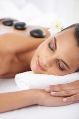 Sleeping, hot stone and woman with massage at spa for wellness, health and back treatment. Self care, cosmetic and young female person relaxing for warm stone back therapy at natural beauty salon.