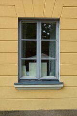 Fototapeta premium Window with with grey frame on a yellow painted stone wall.