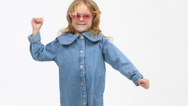 Cheerful little girl in modern clothes having fun, performing freestyle dance moves, on isolated white background. Children's clothing advertising concept