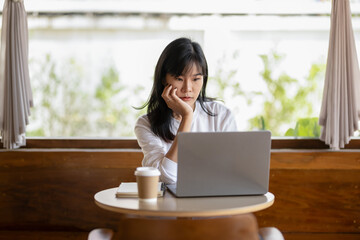 Pensive young adult woman working on a laptop in a cozy home setting, deep in thought..