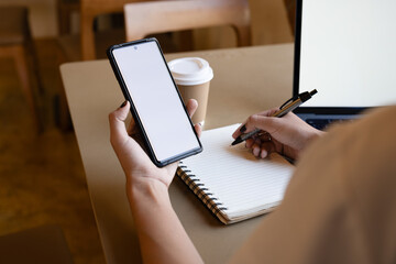 Businesswoman at a workspace with a smartphone and a laptop featuring a white blank screen, ideal for graphic mockups..
