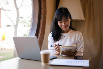 Cheerful young woman with a laptop and notebook, enjoying her work from home setup in a sunny room..