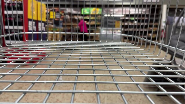 British supermarket view from empty shopping trolley or cart, stopping at bakery. Selective focus on foreground.