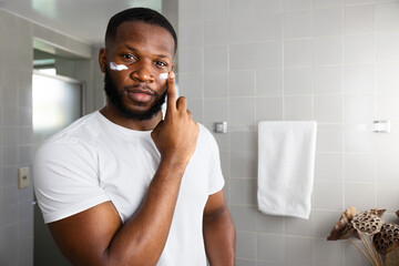 skincare with a handsome African American men wearing a white t-shirt applying moisturizer  in his...