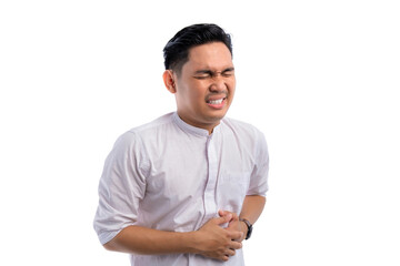 Handsome Asian Muslim man having stomach ache, touching sore stomach isolated on white background....