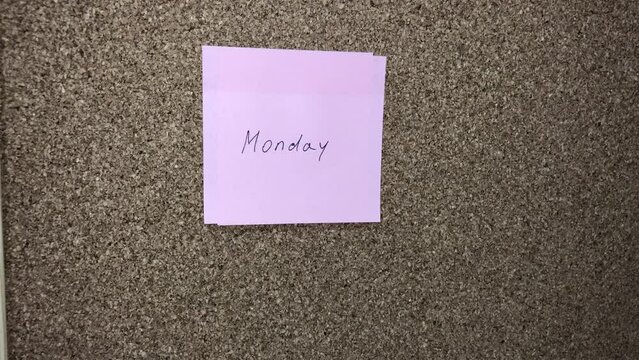 Woman changes pink sticker with the word Sunday to sticker with the word Monday to a cork board.