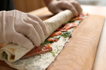Lavash with cheese, vegetables and salmon is wrapped in a roll. Preparation of pita bread.