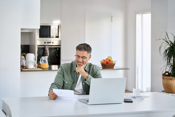 Happy middle aged mature man entrepreneur wearing eyeglasses looking at paper bill checking...