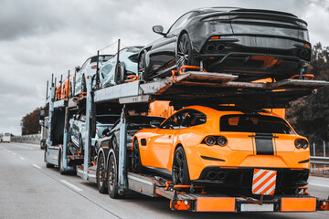 On a two-level hydraulic trailer truck, a load of exotic luxury sport cars gleams with speed and prestige. The ultimate supercars for racing or for showing off are delivered by a transport service.