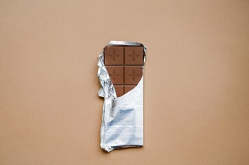 A bar of delicious milk chocolate lies on the table on a light brown background.  Flat lay top view.  Close-up, space for copy text.  The concept of delicious, aromatic desserts.