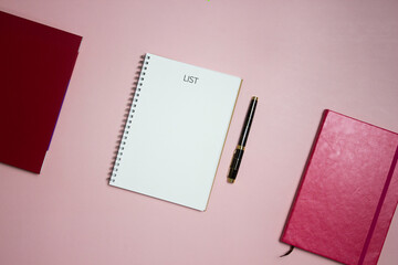 Making list on a blank paper with white and red notebook on a pink background. 