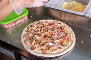 The chef prepares a classic Italian pizza with sausages, mushrooms and tomatoes.