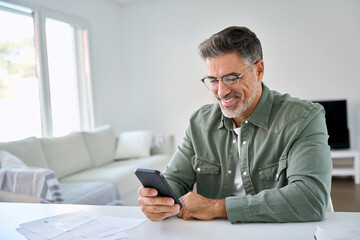 Happy senior older man using smartphone at home. Smiling middle aged mature user looking at mobile...