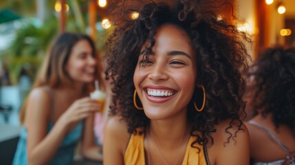 Fototapeta premium A cheerful young woman with curly hair smiling in a tropical setting, surrounded by friends enjoying drinks, embodying joy and friendship