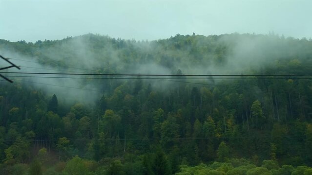 Mountains view outside train window. Passenger train compartment passing by railway bridge and electric wires, Mountain peaks in the morning fog. Traveling by train, nature of Ukraine