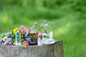 moon amulet, quartz crystals and flowers on stump in forest. Spring summer season. Wiccan, Slavic...