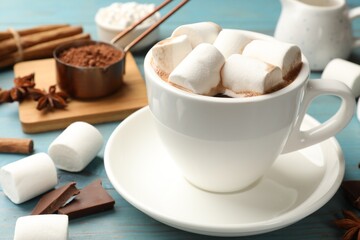 Tasty hot chocolate with marshmallows and ingredients on light blue wooden table, closeup