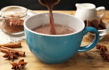 Pouring tasty hot chocolate into cup at wooden table, closeup