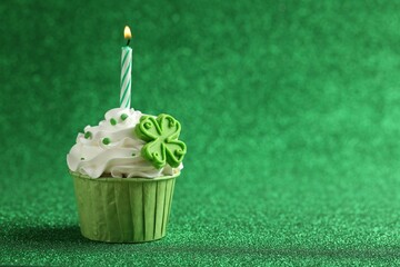 St. Patrick's day party. Tasty cupcake with clover leaf topper and burning candle on shiny green...