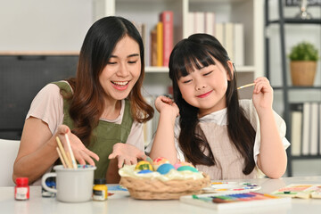 Cute little child girl and mother coloring easter eggs in living room. Preparation for holiday concept