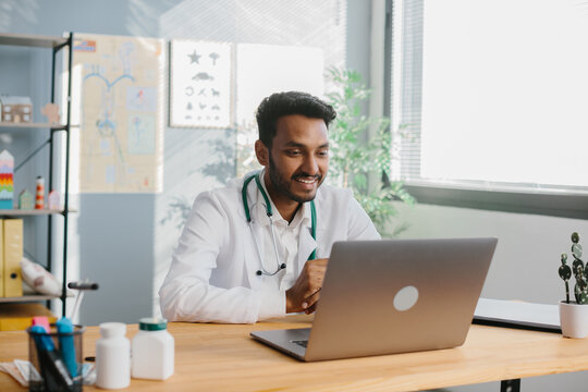An Asian doctor uses a laptop to conduct an online consultation with a patient.