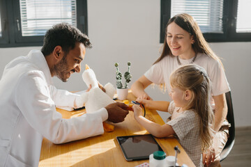 A young pediatrician measures the pulse of a small patient. A mother with a preschool-aged daughter at a doctor's appointment.