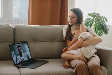 Consultation with a pediatrician online. A young mother with a sick child makes a video call to her...