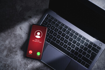 Smartphone receiving unwanted call while resting on laptop. Spam, scam, phishing and fraud concept. Security technology.