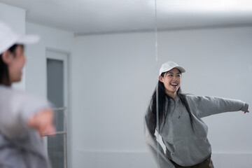 Young female dancer stretching her arms in front of large mirror in studio