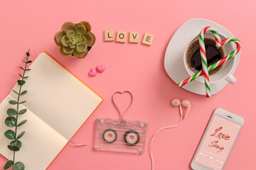 vintage transparent audio cassette magnetic tape in shape of heart, open blank book page, candy cane in the shape of heart on coffee cup, earphones, cactus, mobile phone playing love song on screen